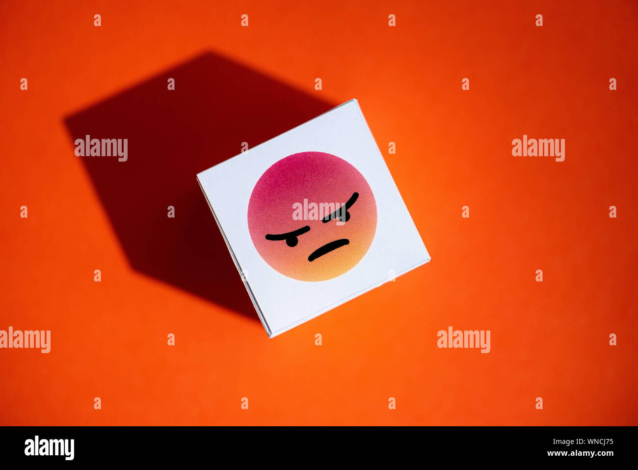 An anger emoji symbol from Facebook Messenger printed on a paper cube, that placed on a orange background. Stock Photo