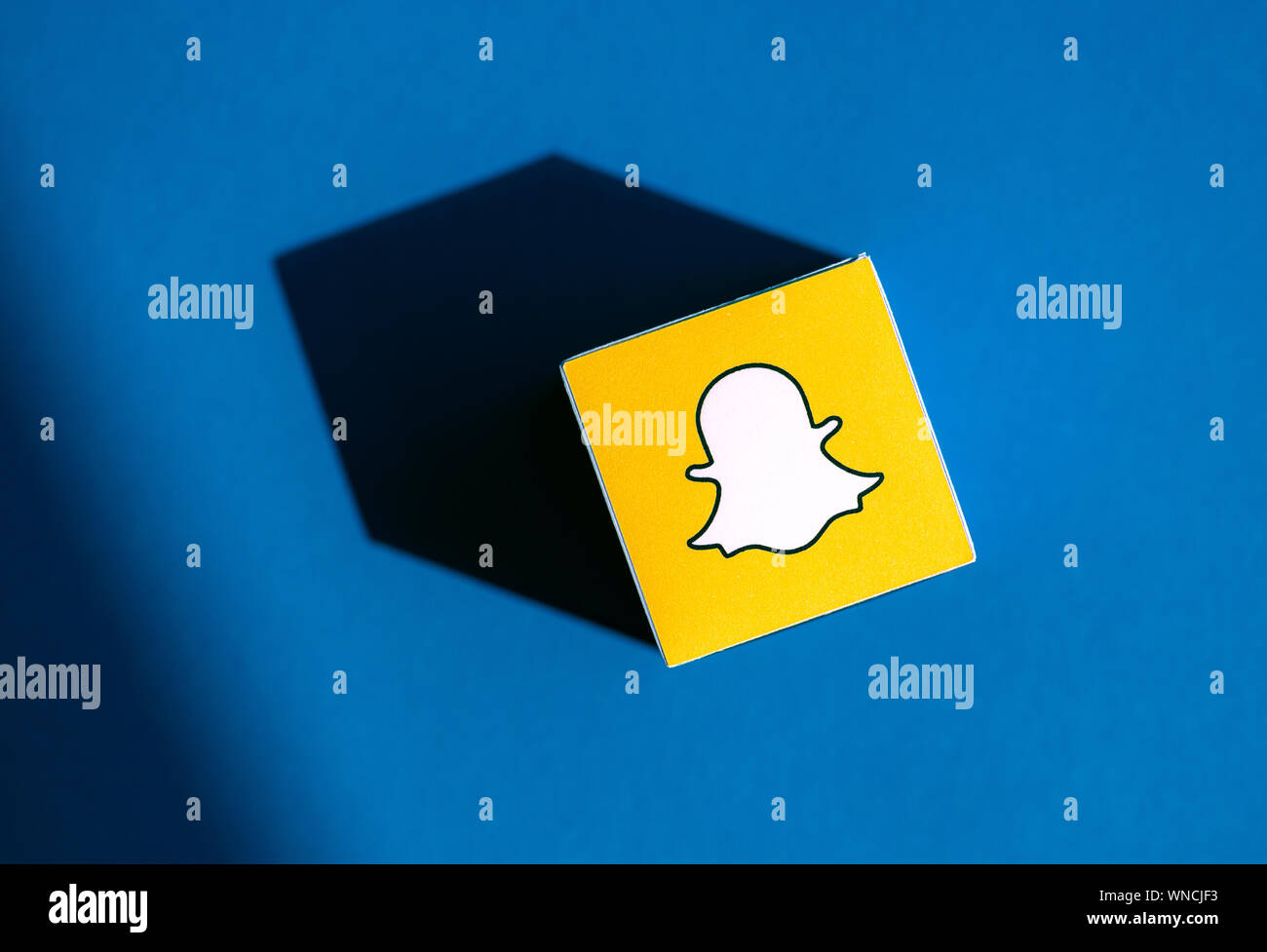 A shot from above of paper cube with the printed logotype of the Snapchat application, that placed on a blue background. Stock Photo