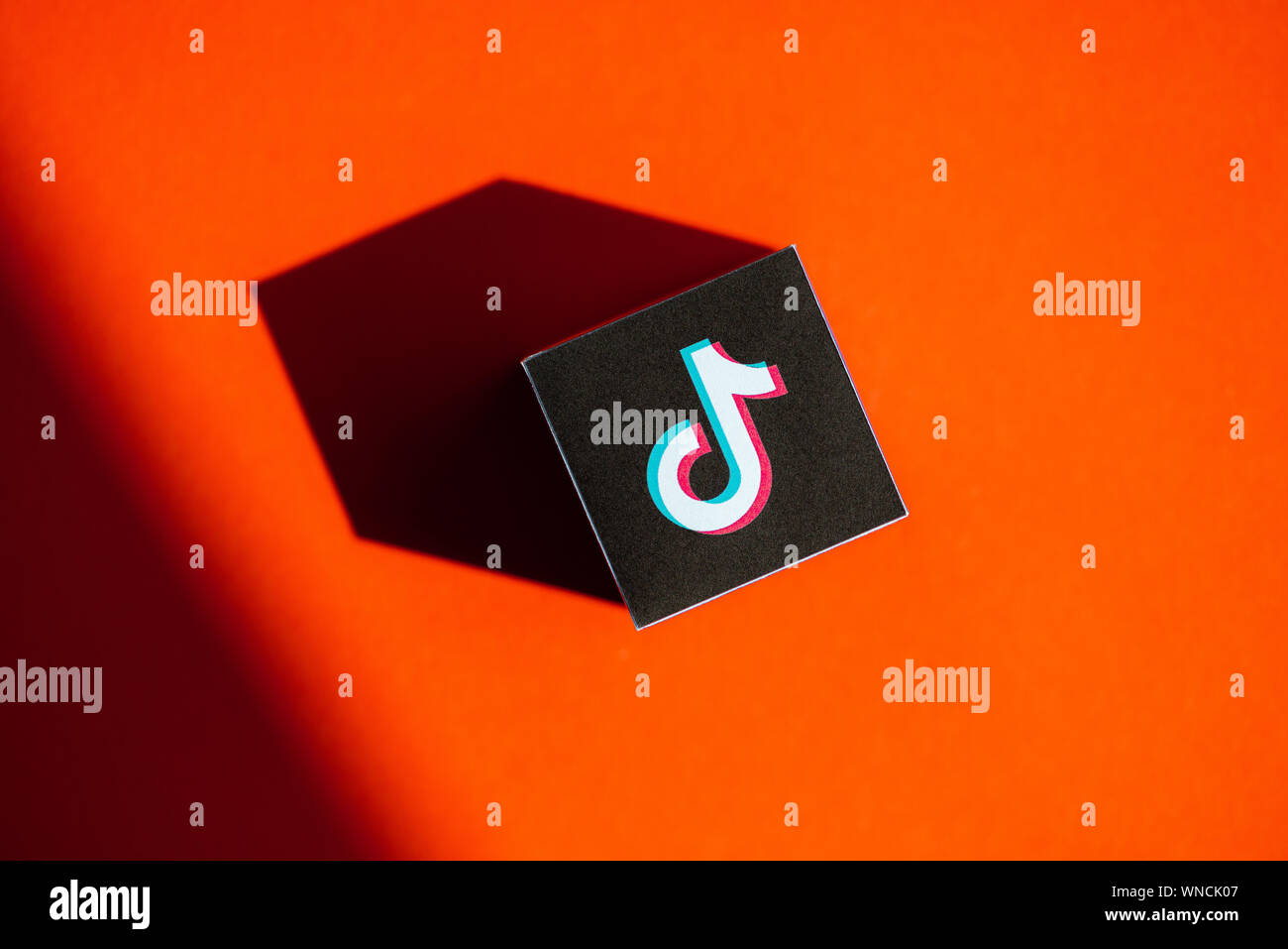 A shot from above of paper cube with the printed logotype of the TikTok application, that placed on an orange background. Stock Photo