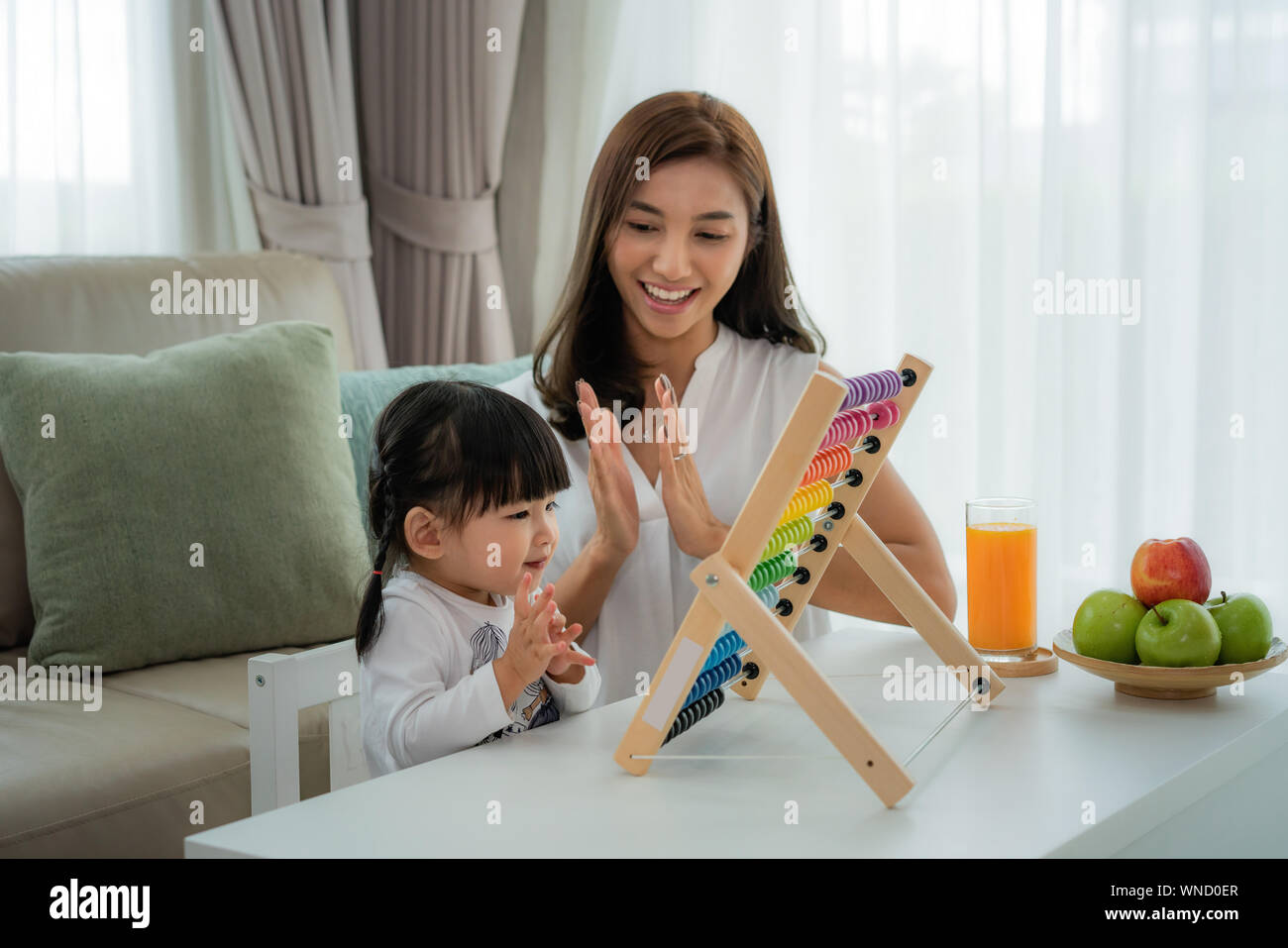 Happy Asian young mother and daughter playing with abacus, early education at home. Stock Photo