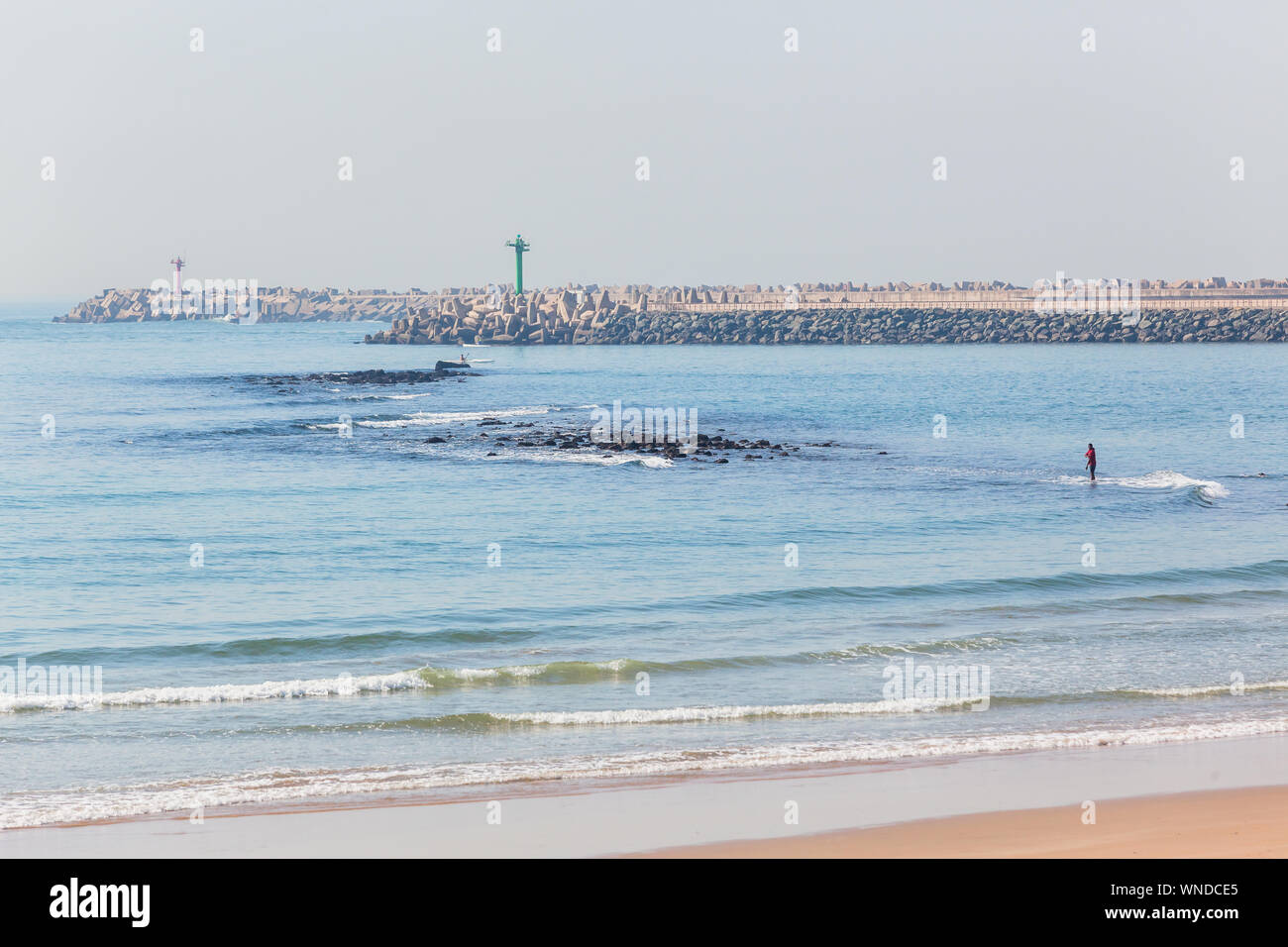 Beach Ocean waters next to harbor piers port entrance at low tide with old submerged rocks landscape. Stock Photo