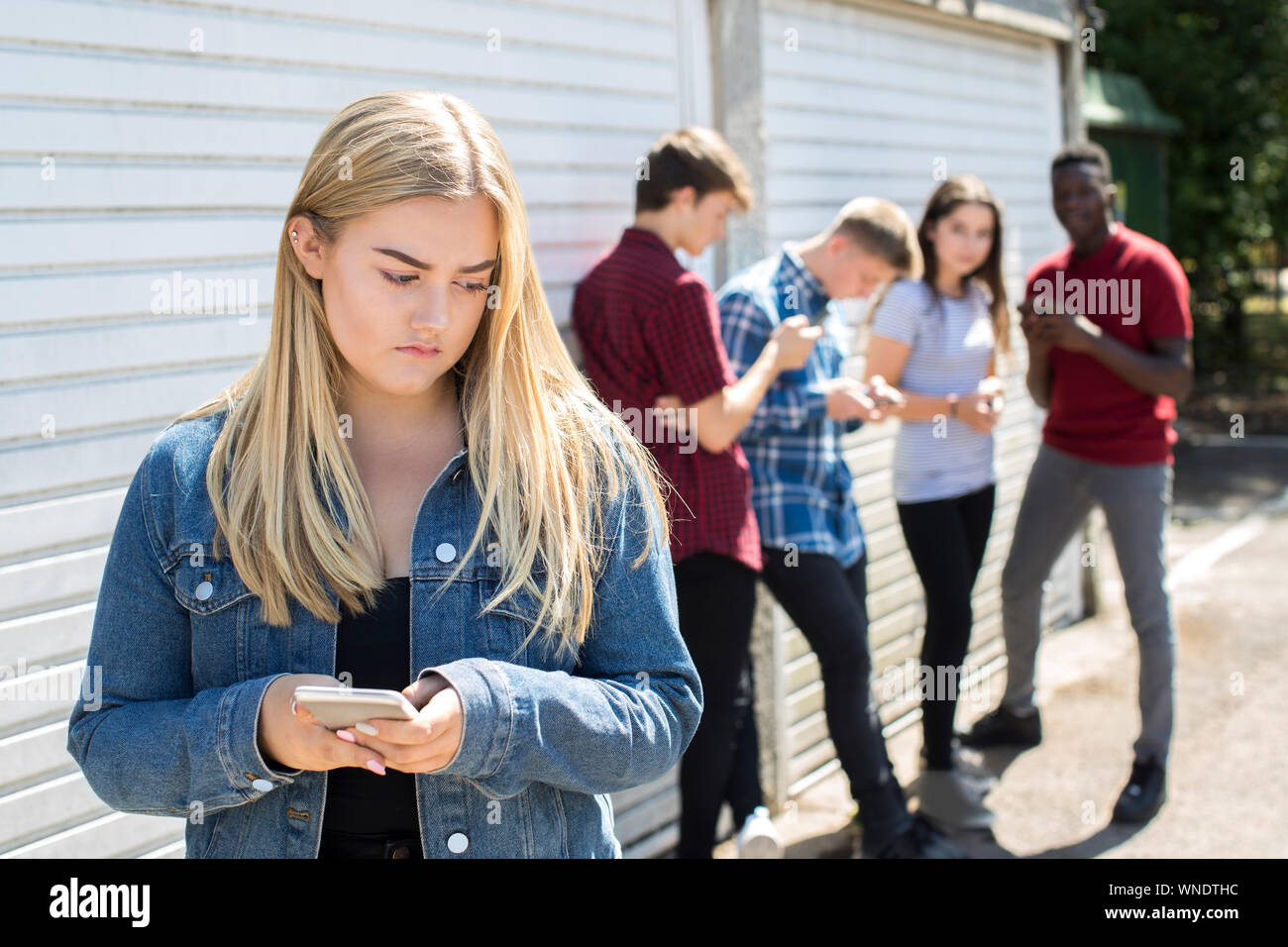 Unhappy Teenage Girl Being Bullied By Text Message Outdoors Stock Photo