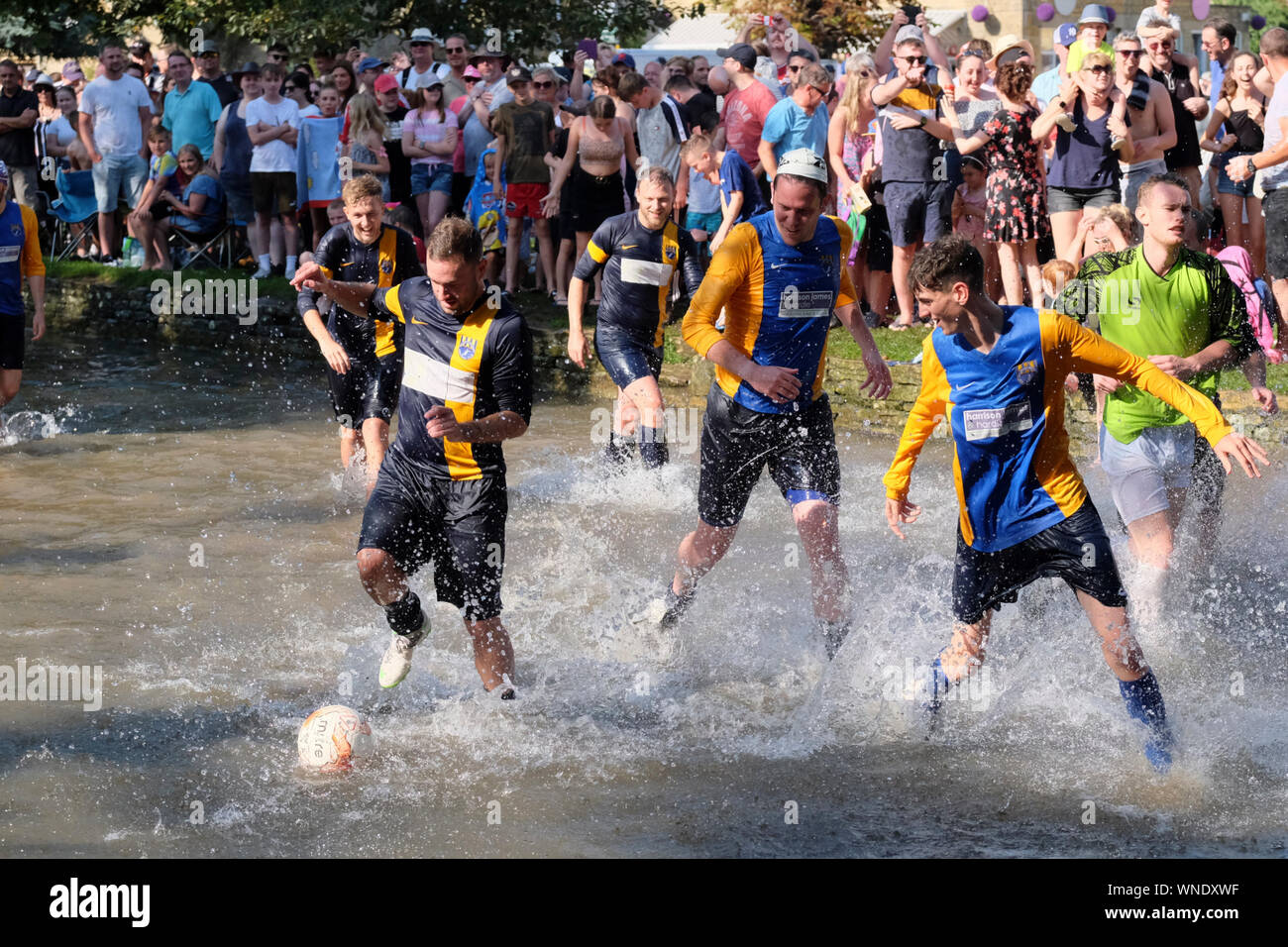 August Bank Holiday festivities in Bourton-on-the Water Gloucestershire UK. The traditional football in the river match. Stock Photo