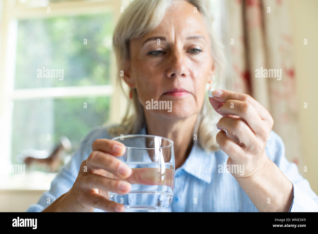Senior Woman Taking Tablet With Glass Of Water At Home Stock Photo