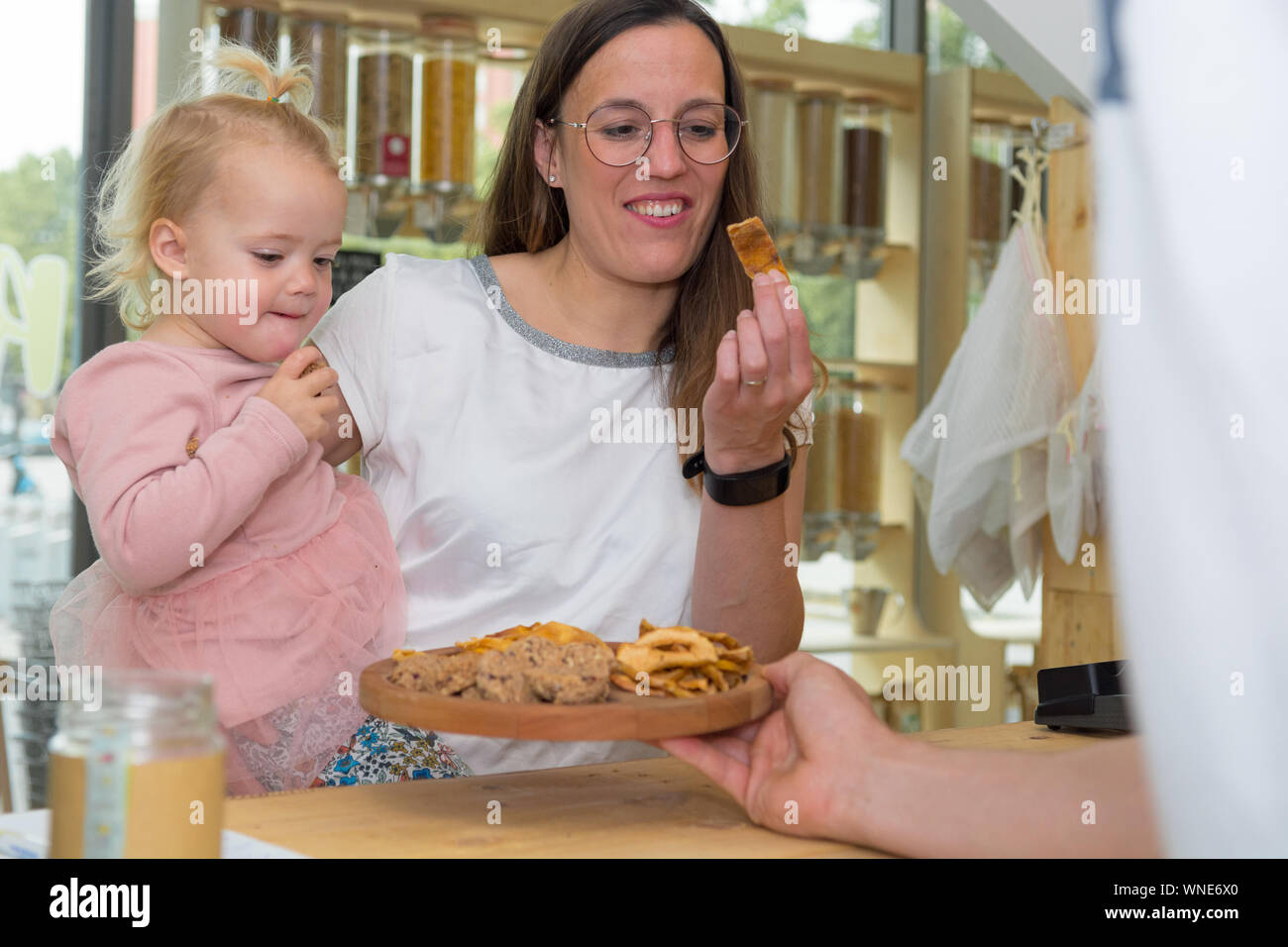 Cute adorable girl trying cookies at organic store with her mother.Degustaion of healthy desert. Stock Photo