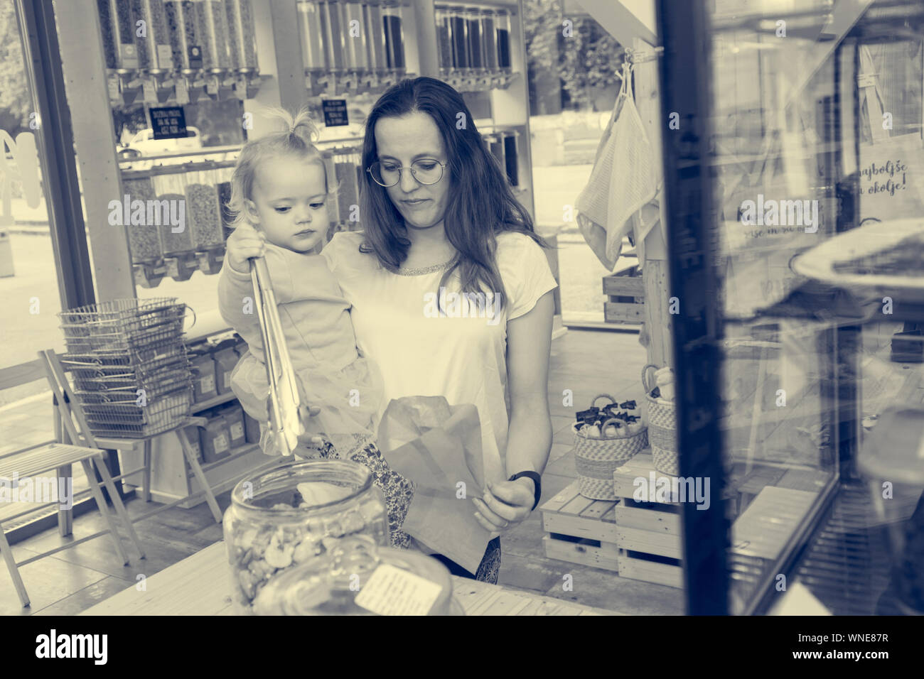 Young mother trying to fill bag with delicious cookies while her mother is eating them. Shopping in zero waste shop. Stock Photo