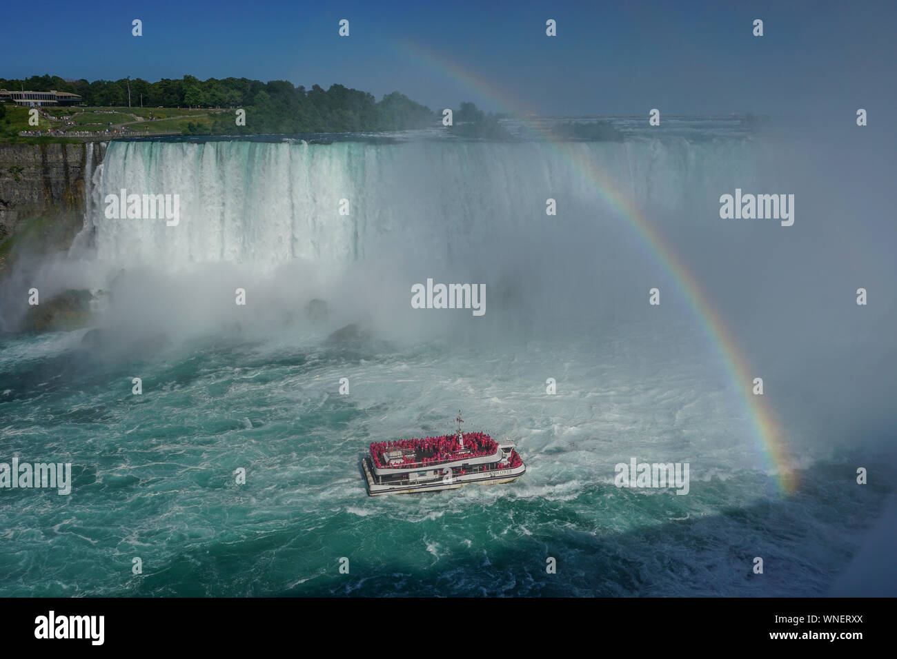 Niagara Falls, Ontario, Canada: A rainbow appears over the Niagara River as a tour boat takes visitors to the foot of the Horseshoe Falls. Stock Photo