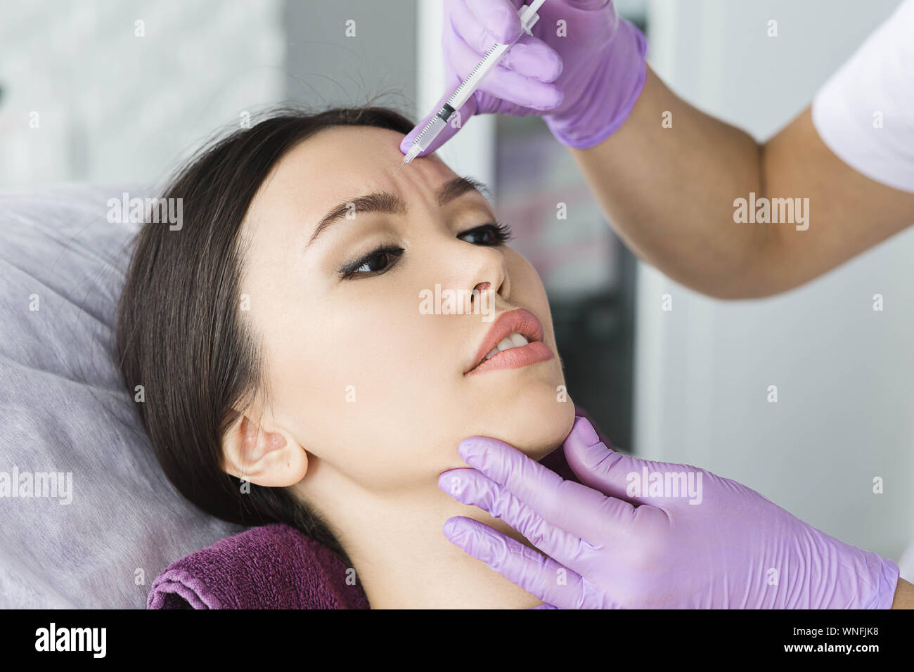 asian woman receiving injection into mimic wrinkle on forehead . Procedure removing wrinkle Stock Photo