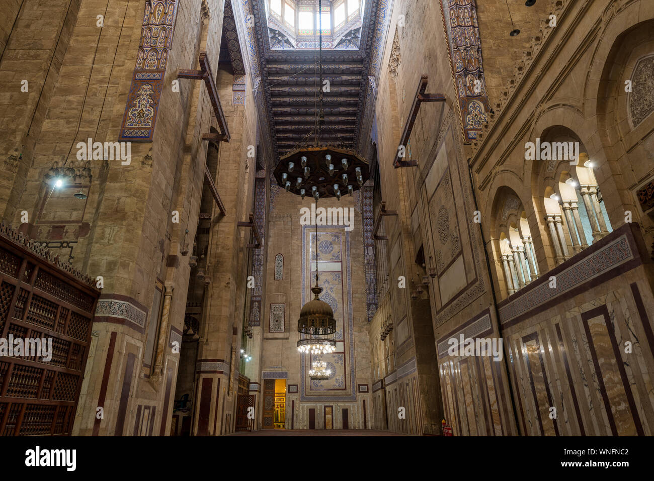 Interior of al Refai mosque with old decorated bricks stone wall, colored marble decorations, wooden ornate ceiling, big brass chandeliers, and wooden latticework door, Cairo, Egypt Stock Photo