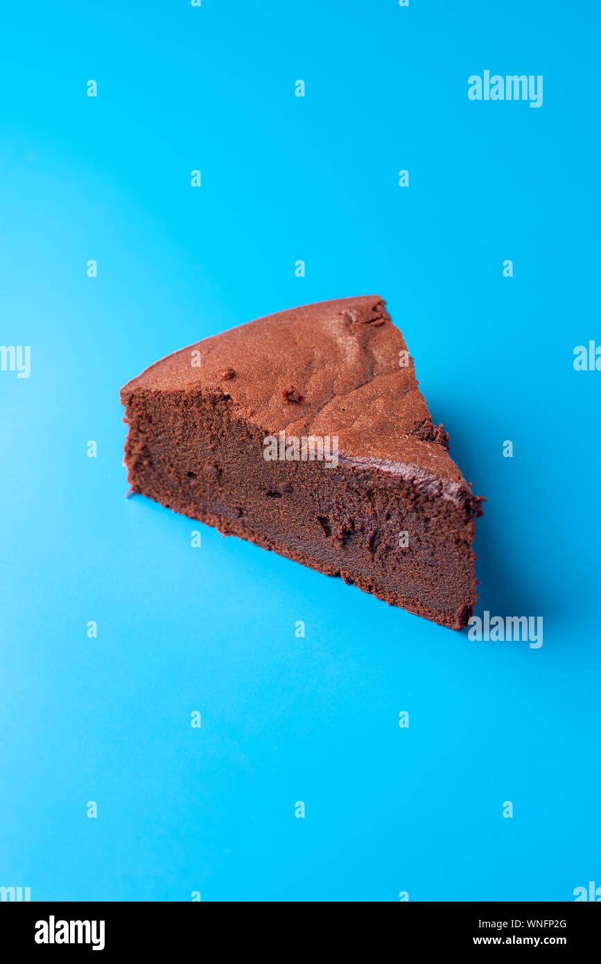 Single piece of Kladdkaka cake, a Swedish sticky chocolate cake. Minimal image of brownie slice on blue background. Scandinavian traditional dessert. Stock Photo