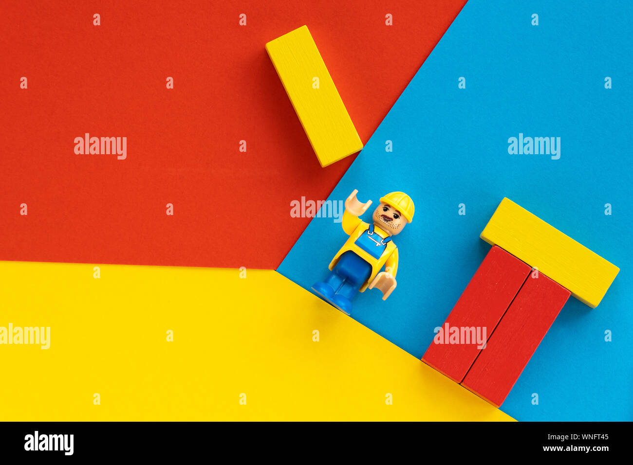 Milan, Italy - August 11 2019: Lego toy of engineer construction worker with helmet building a house. Geometric flat composition on multicoloured Stock Photo