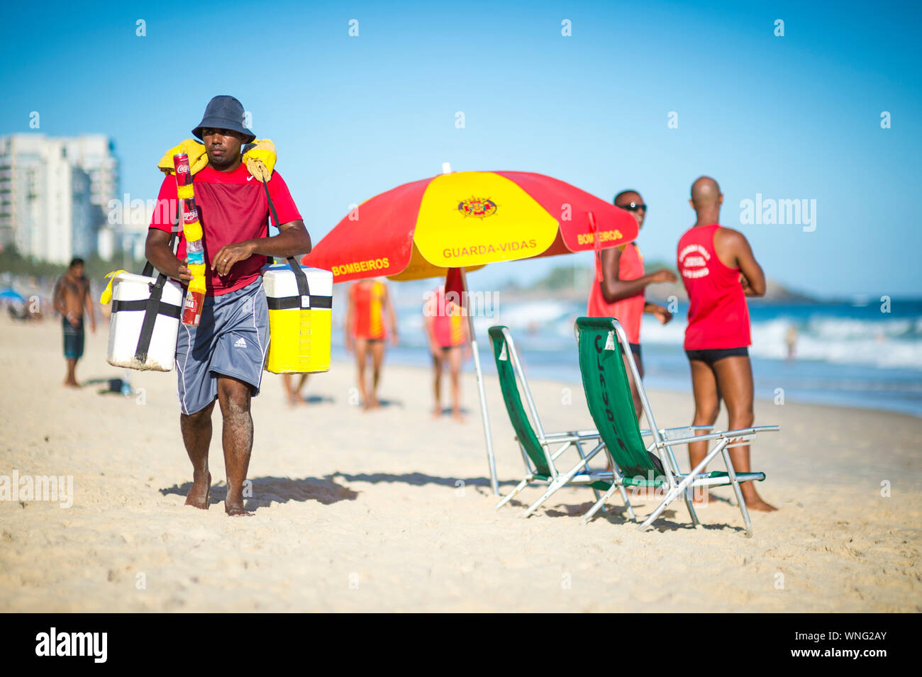RIO DE JANEIRO - MARCH 15, 2018: A beach vendor passes Brazilian lifeguards monitoring heavy surf on Ipanema beach Stock Photo