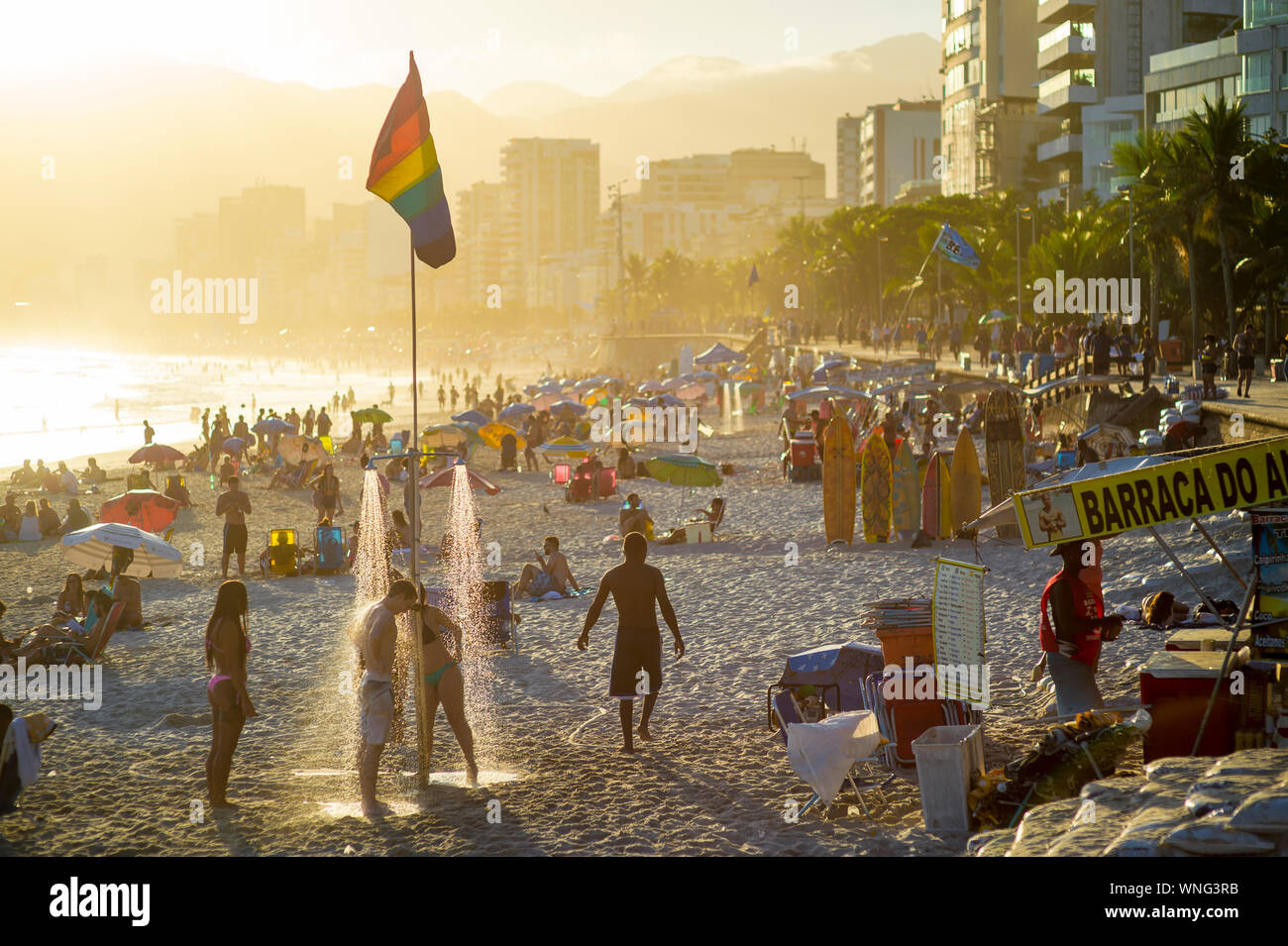 RIO DE JANEIRO - FEBRUARY 14, 2018: Beachgoers shower under a gay pride rainbow flag as the sun sets above LGBTQ-friendly Ipanema Beach. Stock Photo