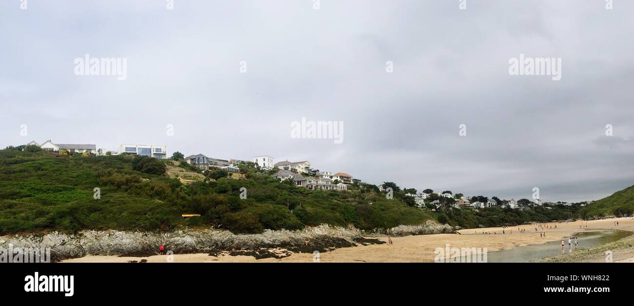 Buildings On Hill By Crantock Beach Against Cloudy Sky Stock Photo
