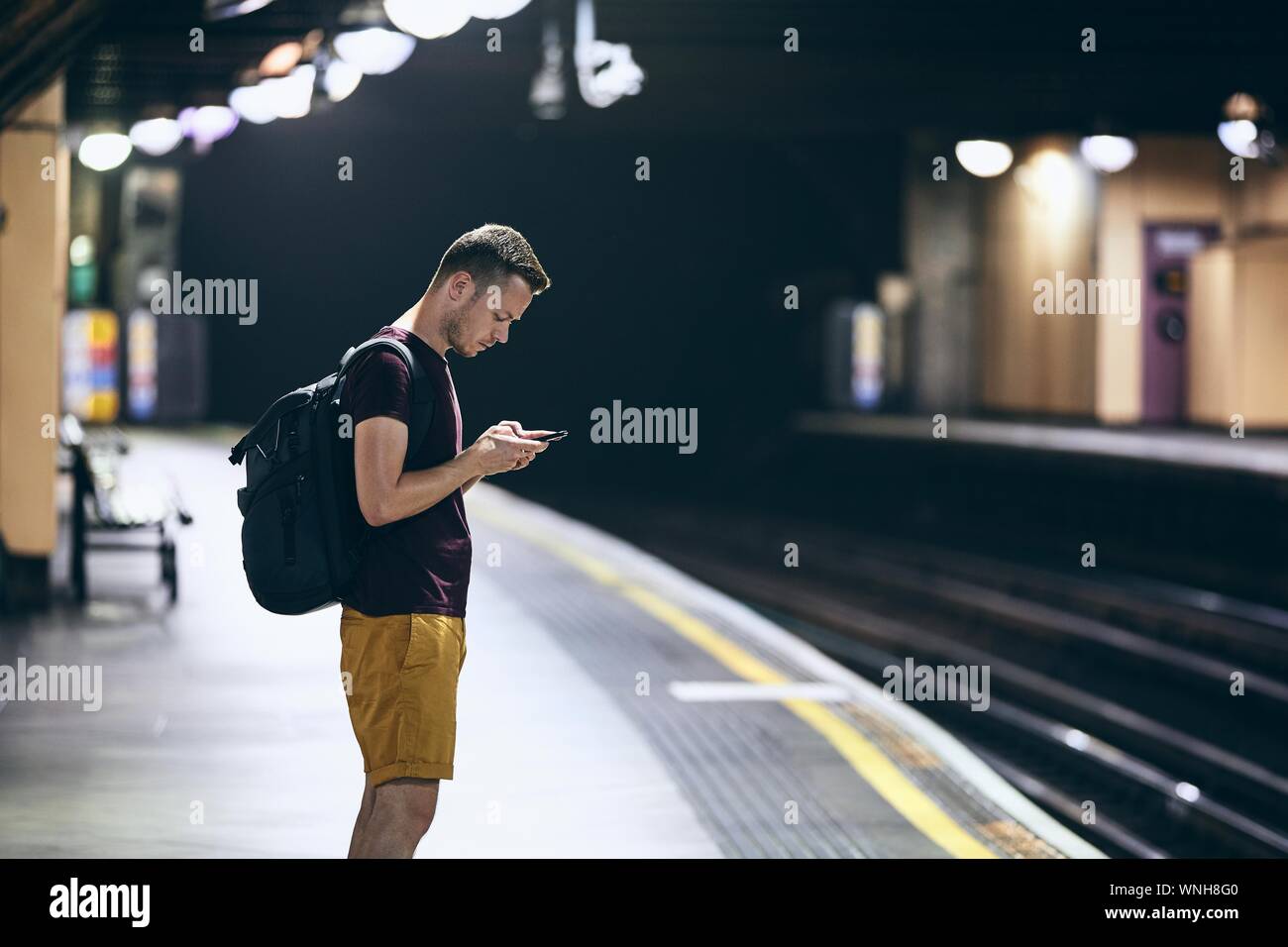 Young man looking at smart phone and waiting on underground station platform. Stock Photo