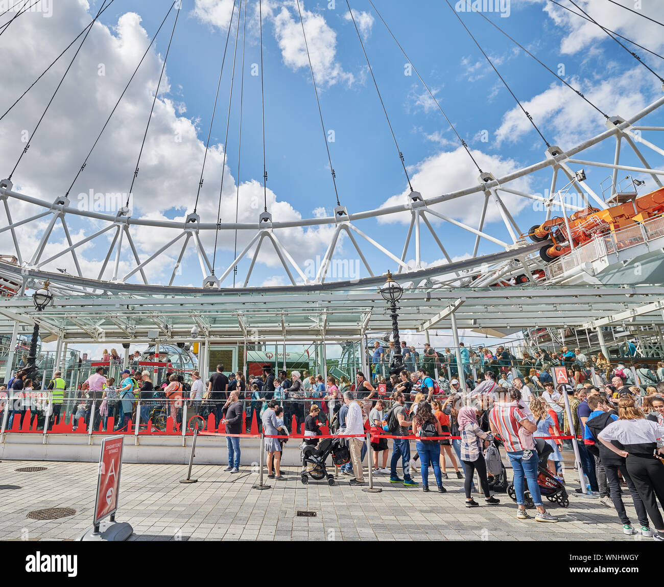 Crowd of people from different nationalities form an orderly queue to enter the London Eye ferris wheel, England, on a summer day. Stock Photo