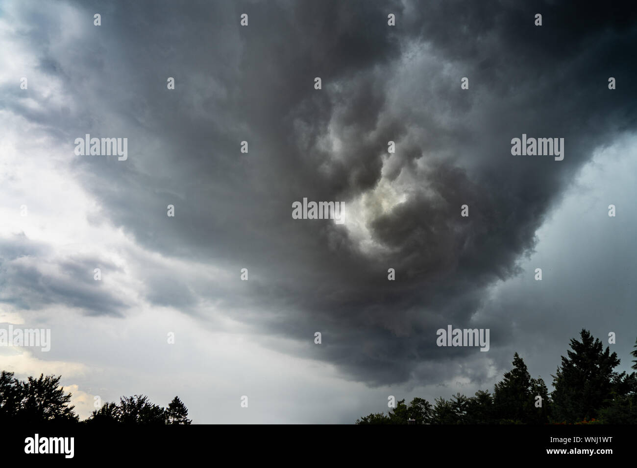 Thundercloud twisting dramatically in itself over treetops Stock Photo
