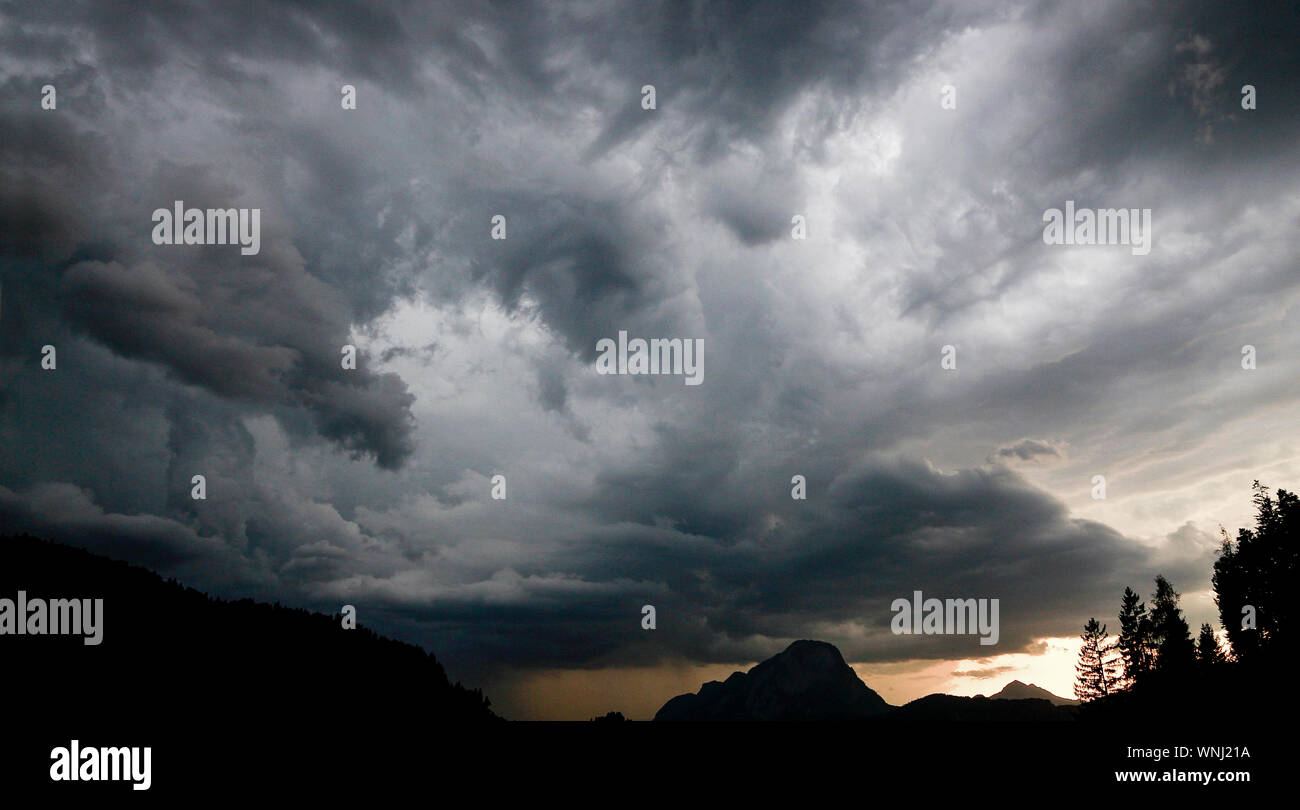 Thunderstorm in the Alps with clouds hanging threating over mountain peak and treetops Stock Photo
