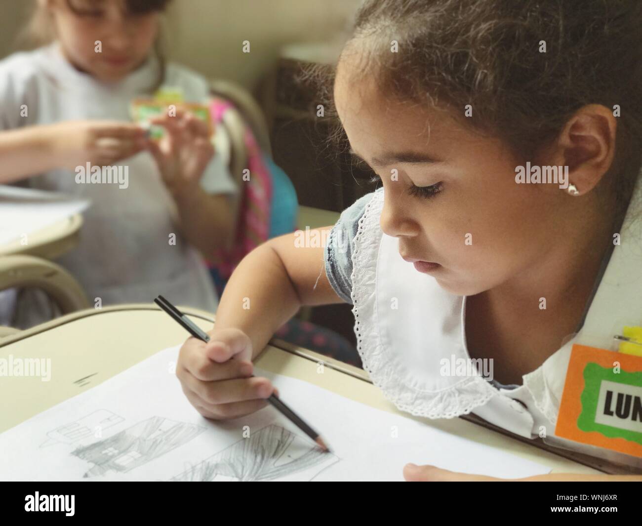 Girl With Name Tag Drawing On Paper At Desk In School Stock Photo