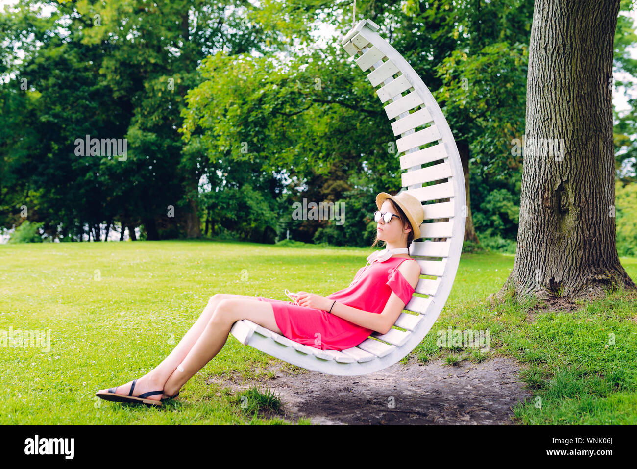 young girl resting on a hanging wooden chair in the garden Stock Photo