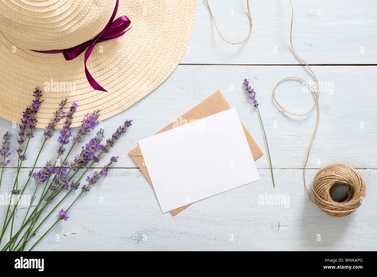 Vintage envelope, blank paper card mockup, lavender flowers, straw hat and twine on rustic blue wooden background. Romantic composition, love love let Stock Photo