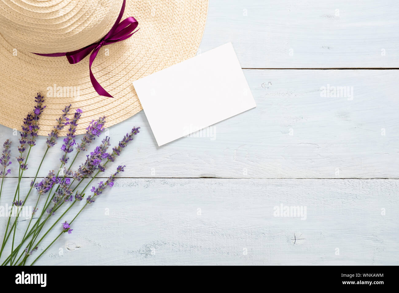 Daisy lavender flowers, straw hat, blank paper card mockup on rustic wooden background. Minimal flat lay style composition, top view, copy space. Summ Stock Photo
