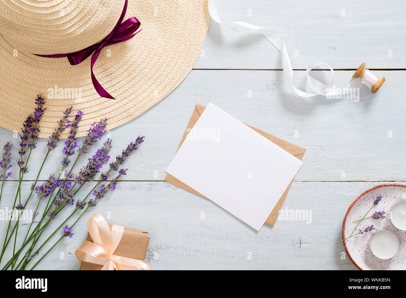 Flatlay composition with straw hat, lavender flowers, paper card mockup, craft envelope, ribbon, gift box, candles. Feminine desk table with romantic Stock Photo