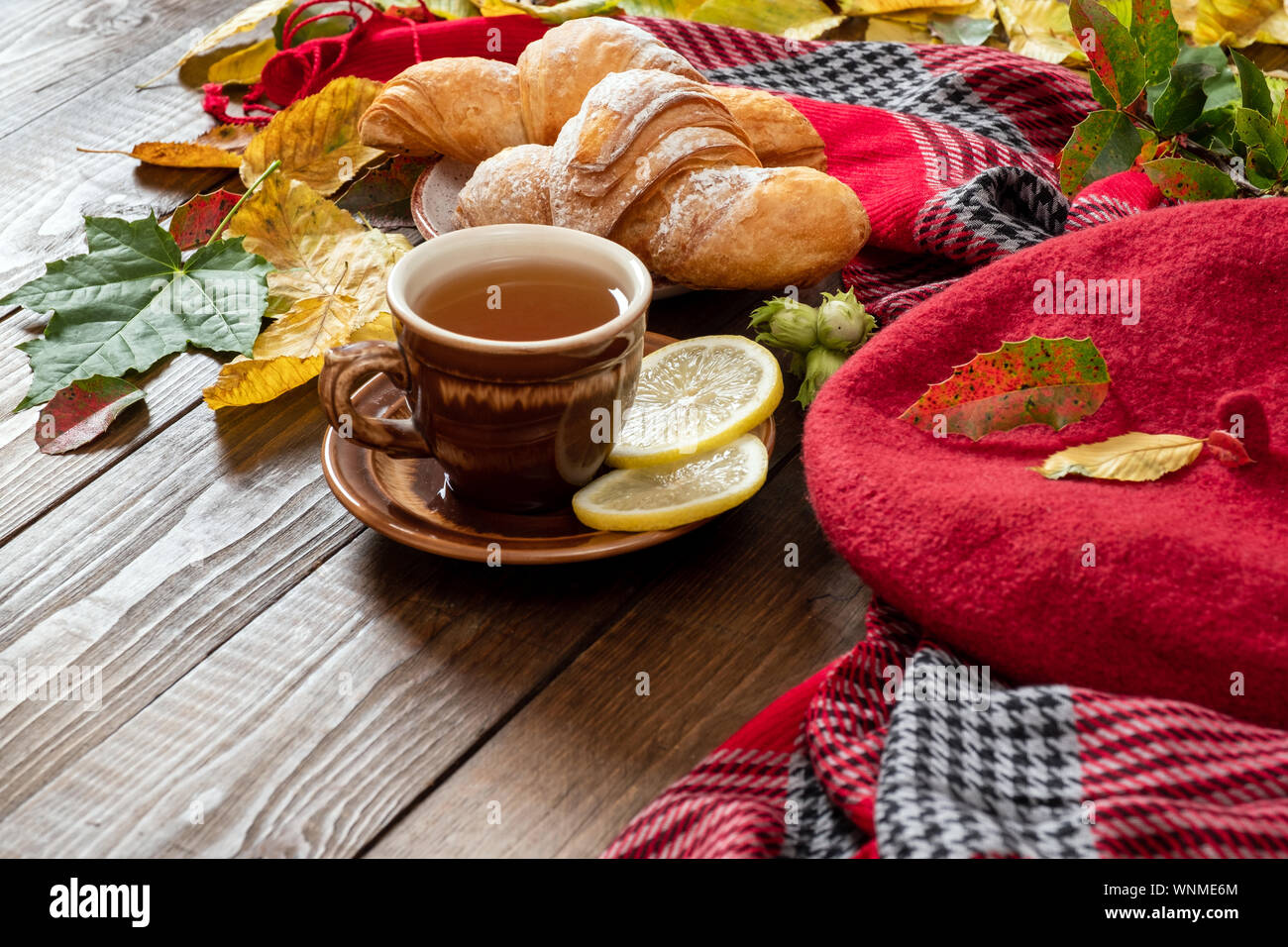 Autumn cozy home morning breakfast concept. Cup of tea, croissants, fallen  leaves, red beret and feminine scarf on wooden desk table Stock Photo -  Alamy, image size:1300x956
