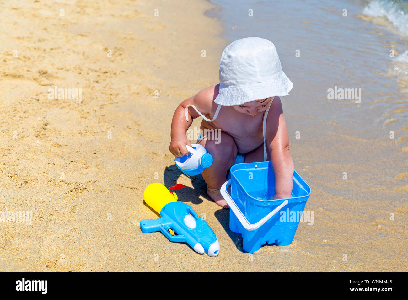 Baby boy playing on the beach with blue bucket and sand toys. One year
