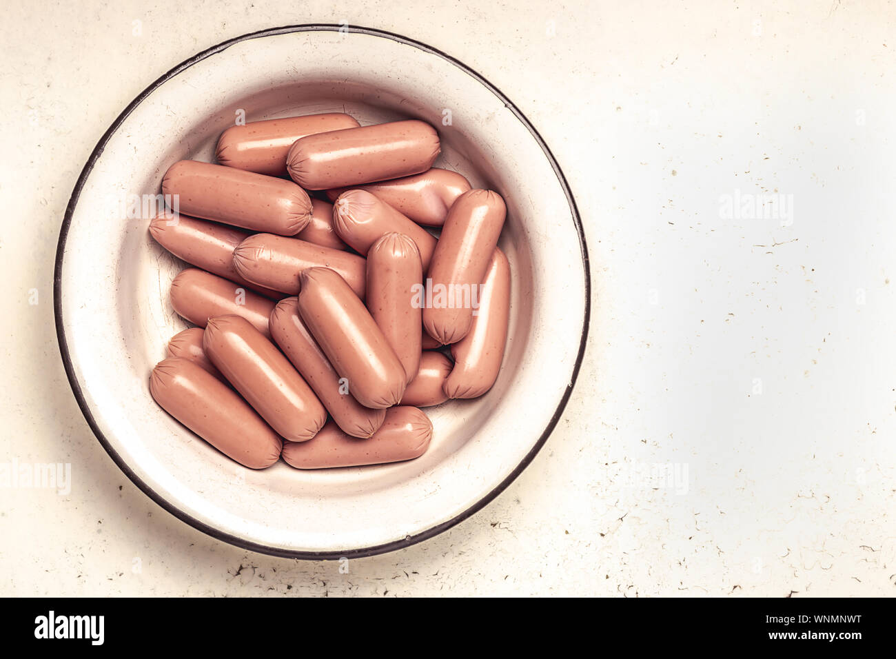 raw sausages in old metal bowl on cracked white background. Top view Stock Photo