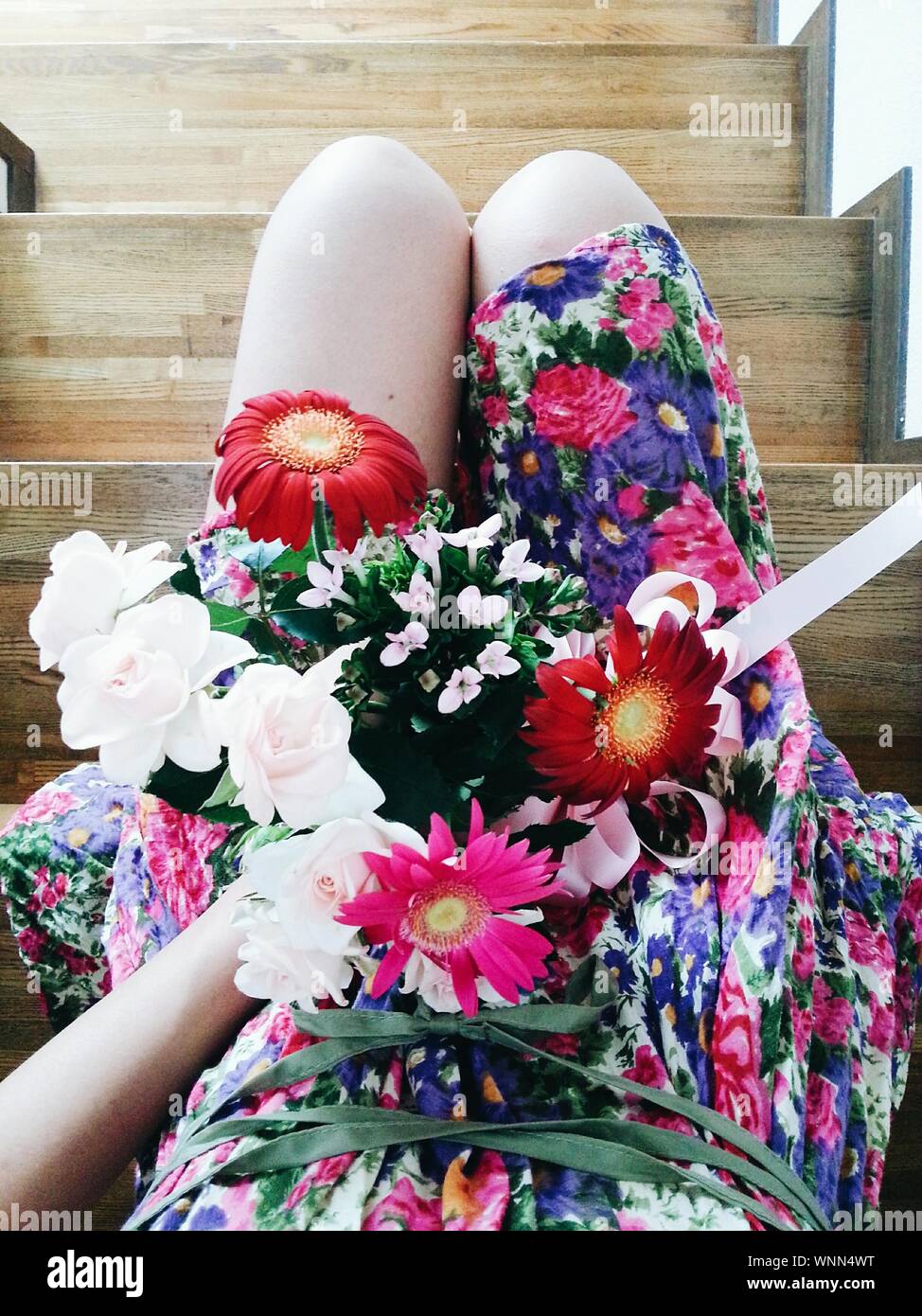 Low Section Of Woman Wearing Floral Dress Holding Flowers While Sitting On Steps Stock Photo