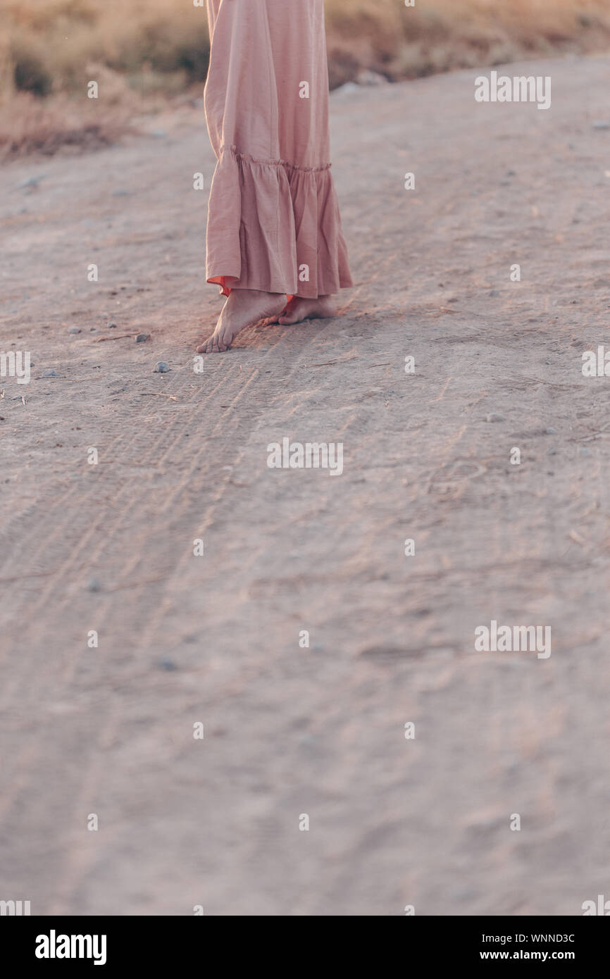 feet of a woman in a pink dress walking on the sand during sunset Stock Photo