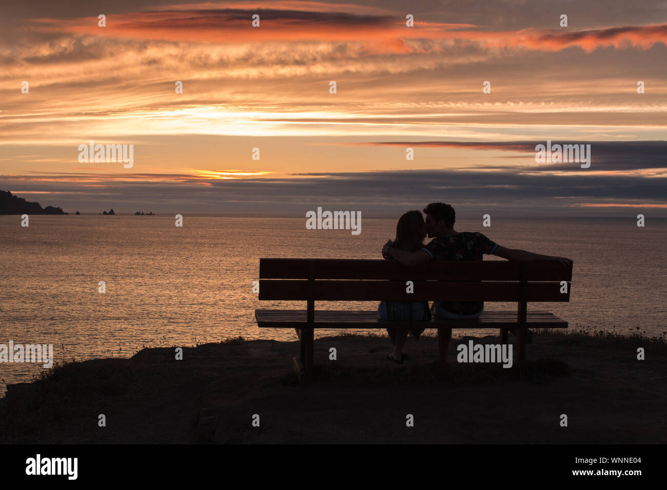 couple in love sitting on a bench watching a beautiful sunset Stock Photo