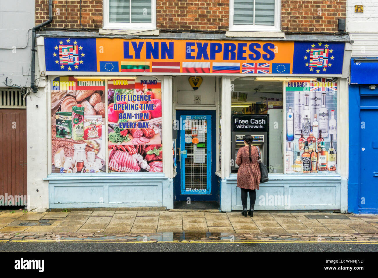 Woman using a free withdrawals cash machine at the Lynn Express Eastern European supermarket in King's Lynn, Norfolk. Stock Photo