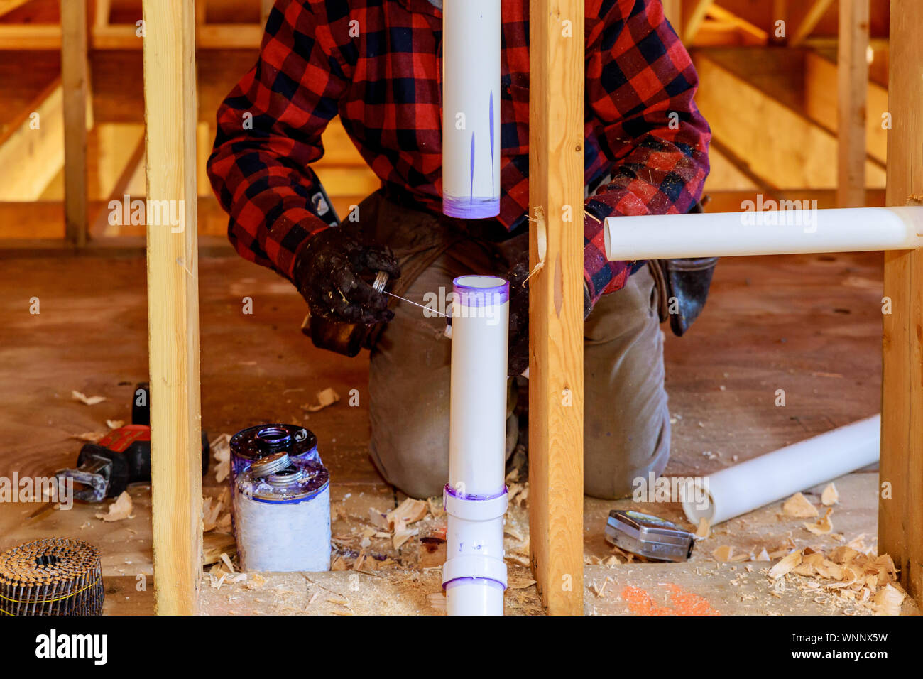 Plumber applying glue to PVC pipe in new home under construction Stock