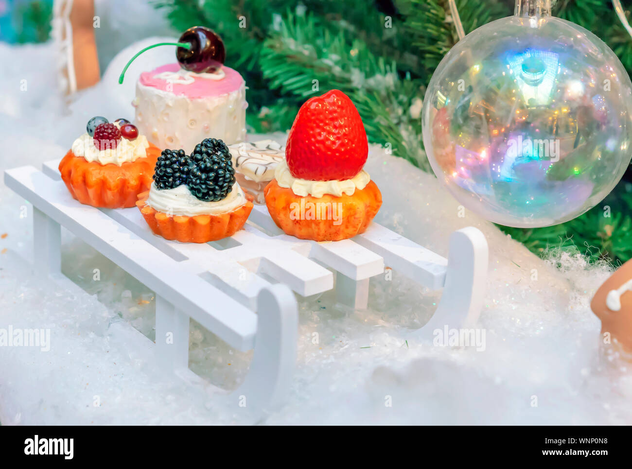 Decorations in the form of a variety of cakes on the background of the Christmas tree. Stock Photo