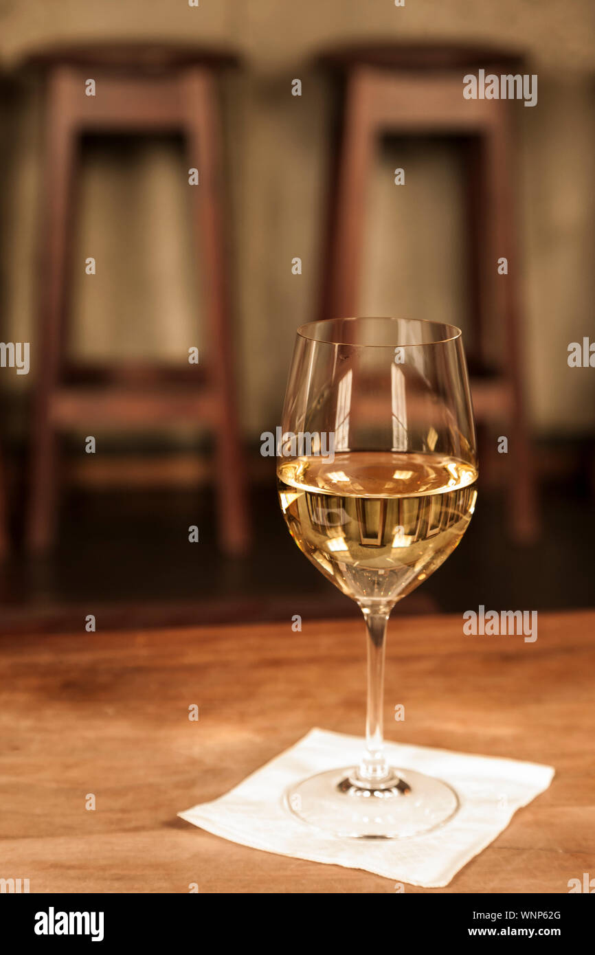 Glass of white wine Chardonnay on table in upscale bar restaurant with barstools in background. Stock Photo
