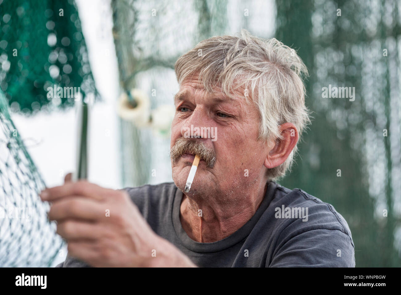 Commercial fisherman smoking and mending nets Stock Photo