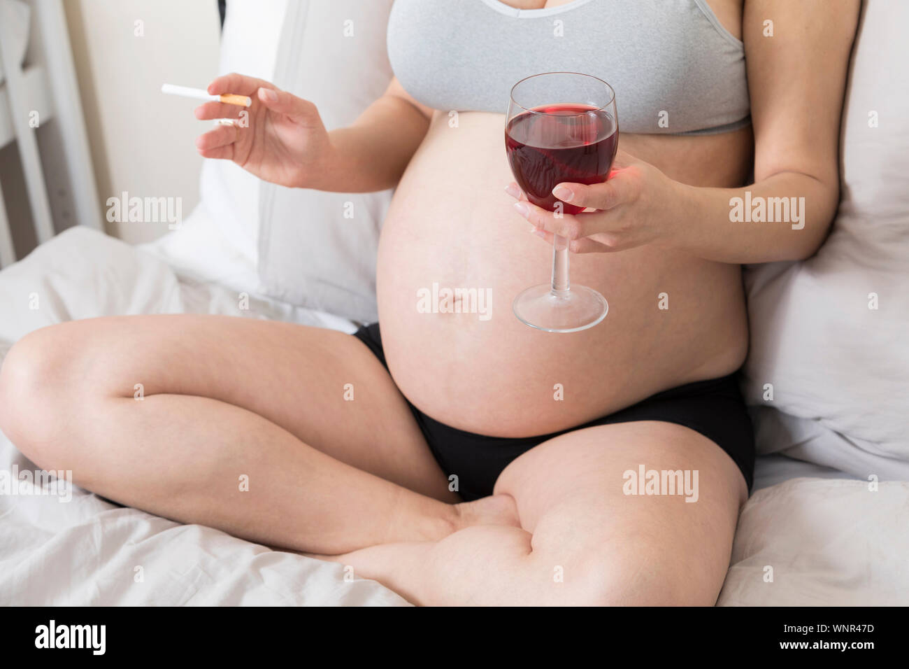 Pregnant woman smoking a cigarette and drinking alcohol, Woman in pregnancy with tobacco and glass of wine Stock Photo