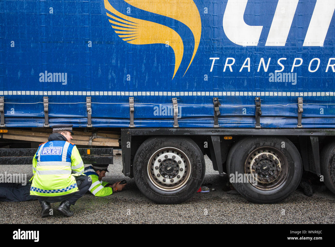 London, UK. 6 September, 2019. Metropolitan Police officers monitor an activist locked beneath a truck making a delivery to ExCel London for DSEI, the world’s largest arms fair. The road remained blocked for several hours. The fifth day of protests against the arms fair was themed as Stop The Arms Fair: Stop Climate Change in order to highlight links between the fossil fuel and arms industries. Credit: Mark Kerrison/Alamy Live News Stock Photo