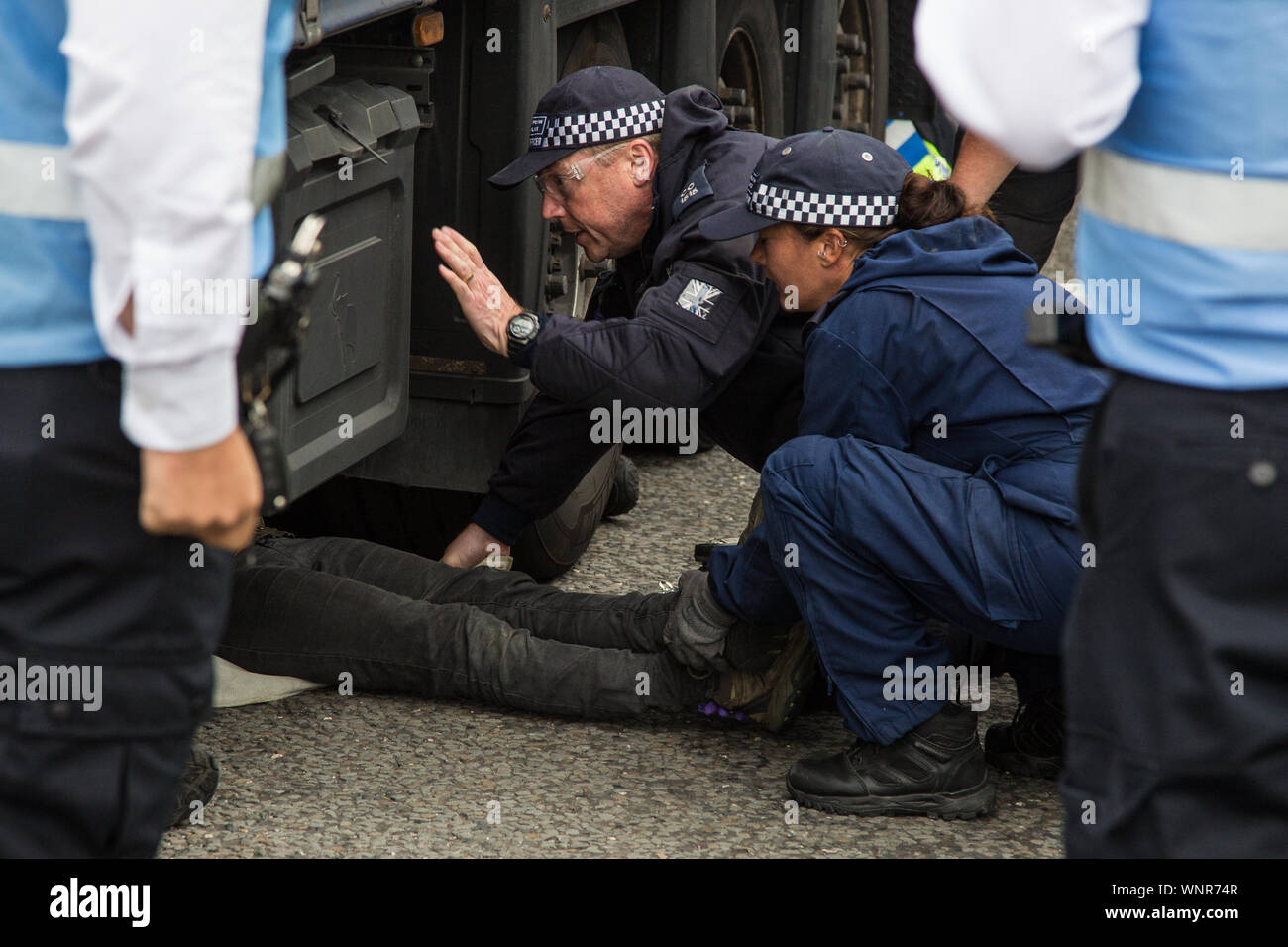 London, UK. 6 September, 2019. Metropolitan Police officers remove an activist who had locked herself beneath a truck making a delivery to ExCel London for DSEI, the world’s largest arms fair. The road remained blocked for several hours. The fifth day of protests against the arms fair was themed as Stop The Arms Fair: Stop Climate Change in order to highlight links between the fossil fuel and arms industries. Credit: Mark Kerrison/Alamy Live News Stock Photo