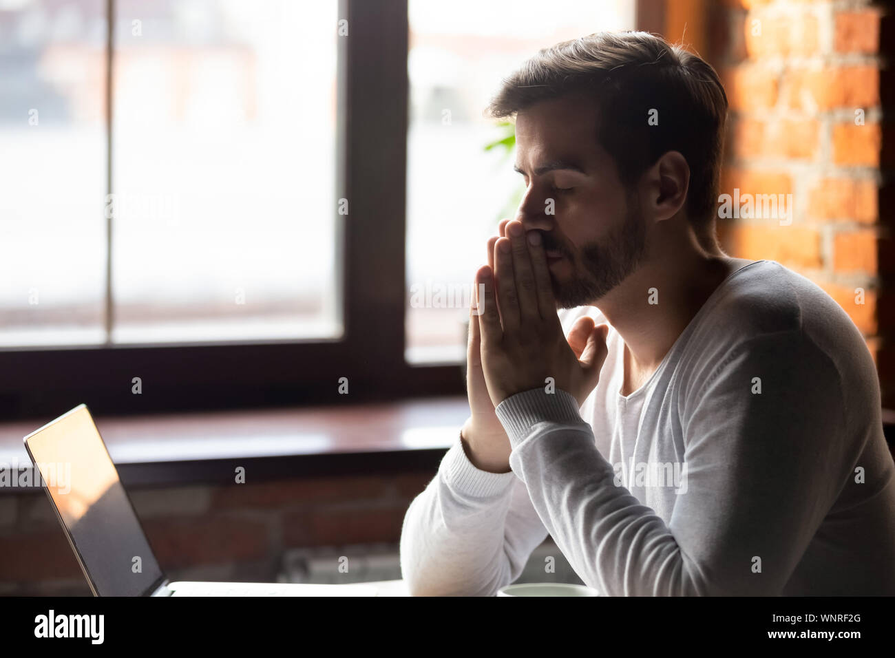 Worried man thinking about problem puts hands together in prayer Stock Photo