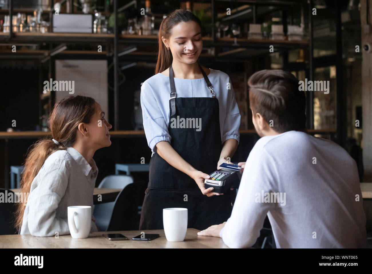 Customer paying by contactless credit card, attractive waitress holding reader Stock Photo
