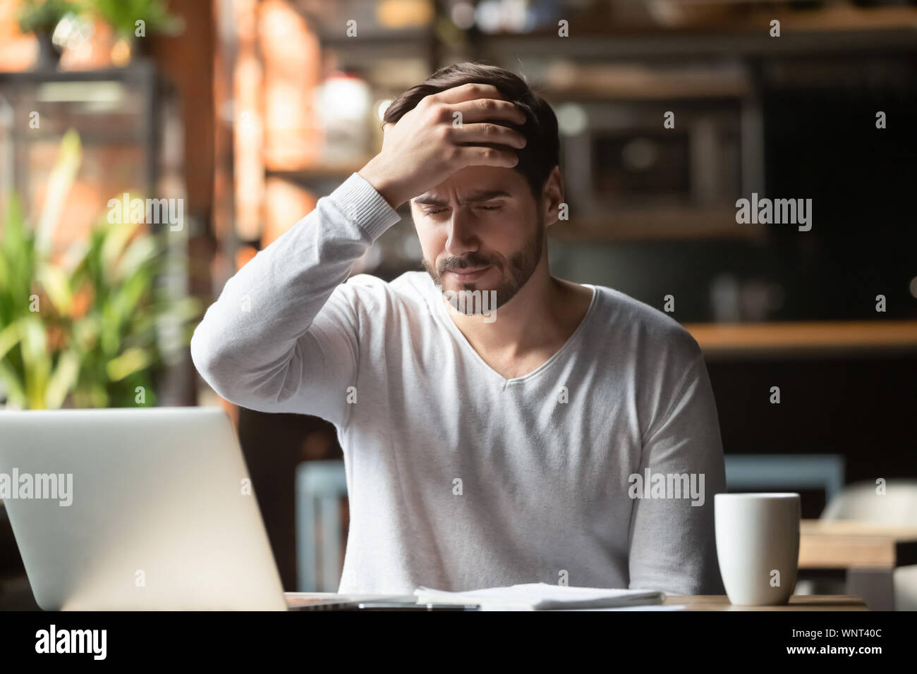 Upset man working in cafe, suffering from headache, touching forehead Stock Photo