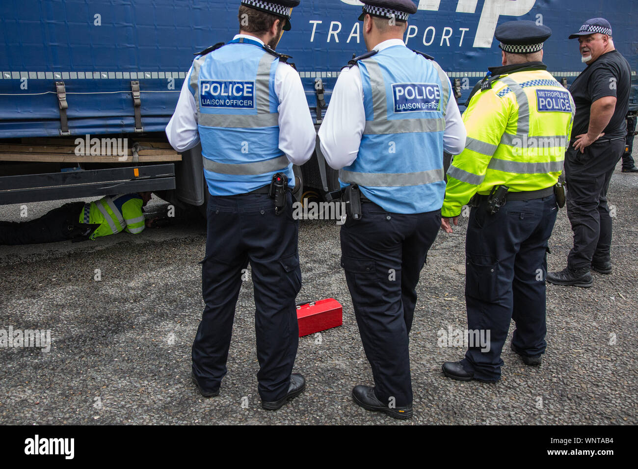 London, UK. 6 September, 2019. Metropolitan Police officers work to remove an activist locked beneath a truck making a delivery to ExCel London for DSEI, the world’s largest arms fair. The road remained blocked for several hours. The fifth day of protests against the arms fair was themed as Stop The Arms Fair: Stop Climate Change in order to highlight links between the fossil fuel and arms industries. Credit: Mark Kerrison/Alamy Live News Stock Photo