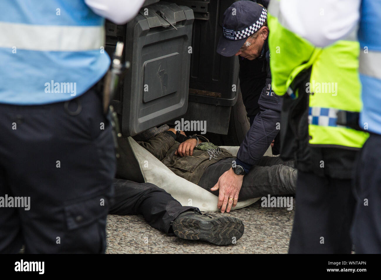London, UK. 6 September, 2019. Metropolitan Police officers remove and arrest an activist who had locked herself beneath a truck making a delivery to ExCel London for DSEI, the world’s largest arms fair. The road remained blocked for several hours. The fifth day of protests against the arms fair was themed as Stop The Arms Fair: Stop Climate Change in order to highlight links between the fossil fuel and arms industries. Credit: Mark Kerrison/Alamy Live News Stock Photo