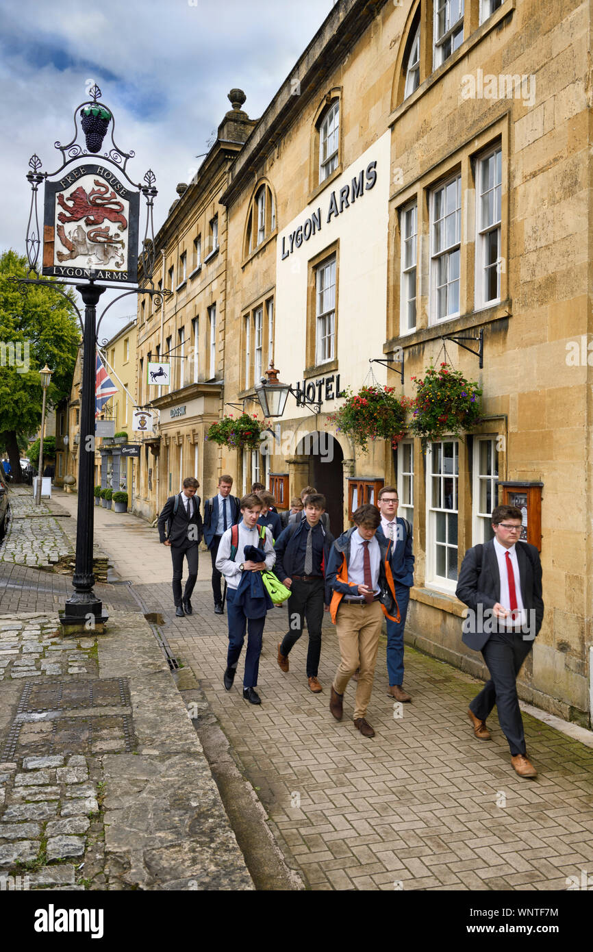 Schoolboys on lunch break walking Past 16th Century Lygon Arms Hotel on High street in Chipping Campden Cotswold England Stock Photo