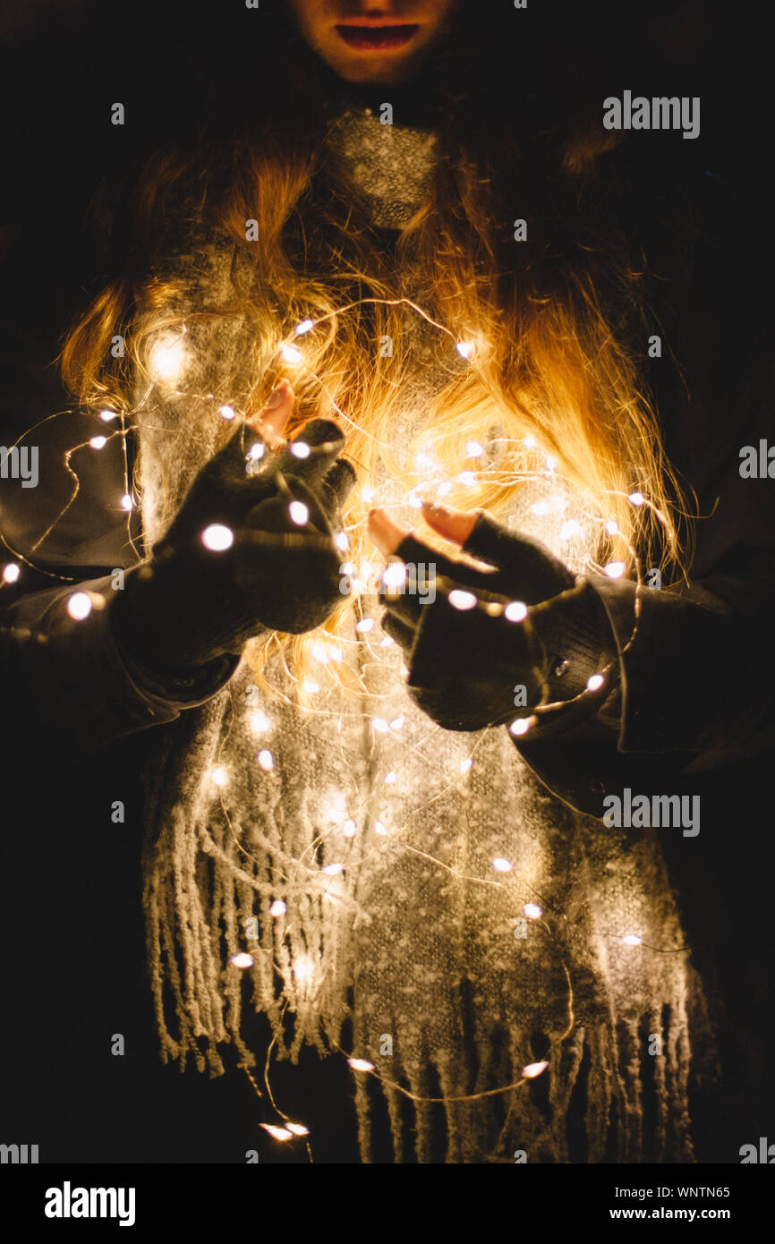 Young woman holding Christmas lights outdoors in the dark Stock Photo