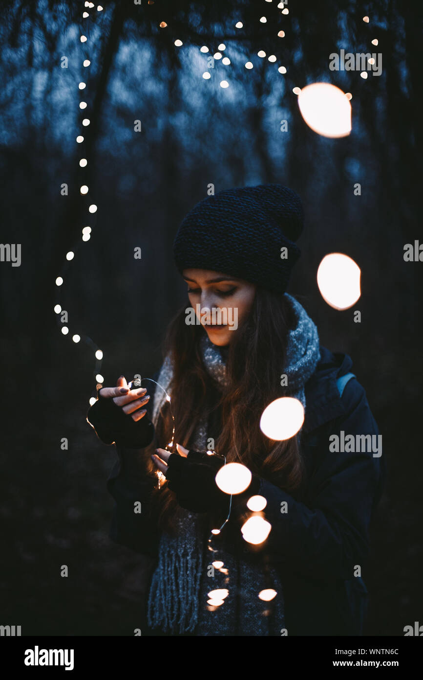 Young hipster woman holding Christmas lights while standing in park Stock Photo