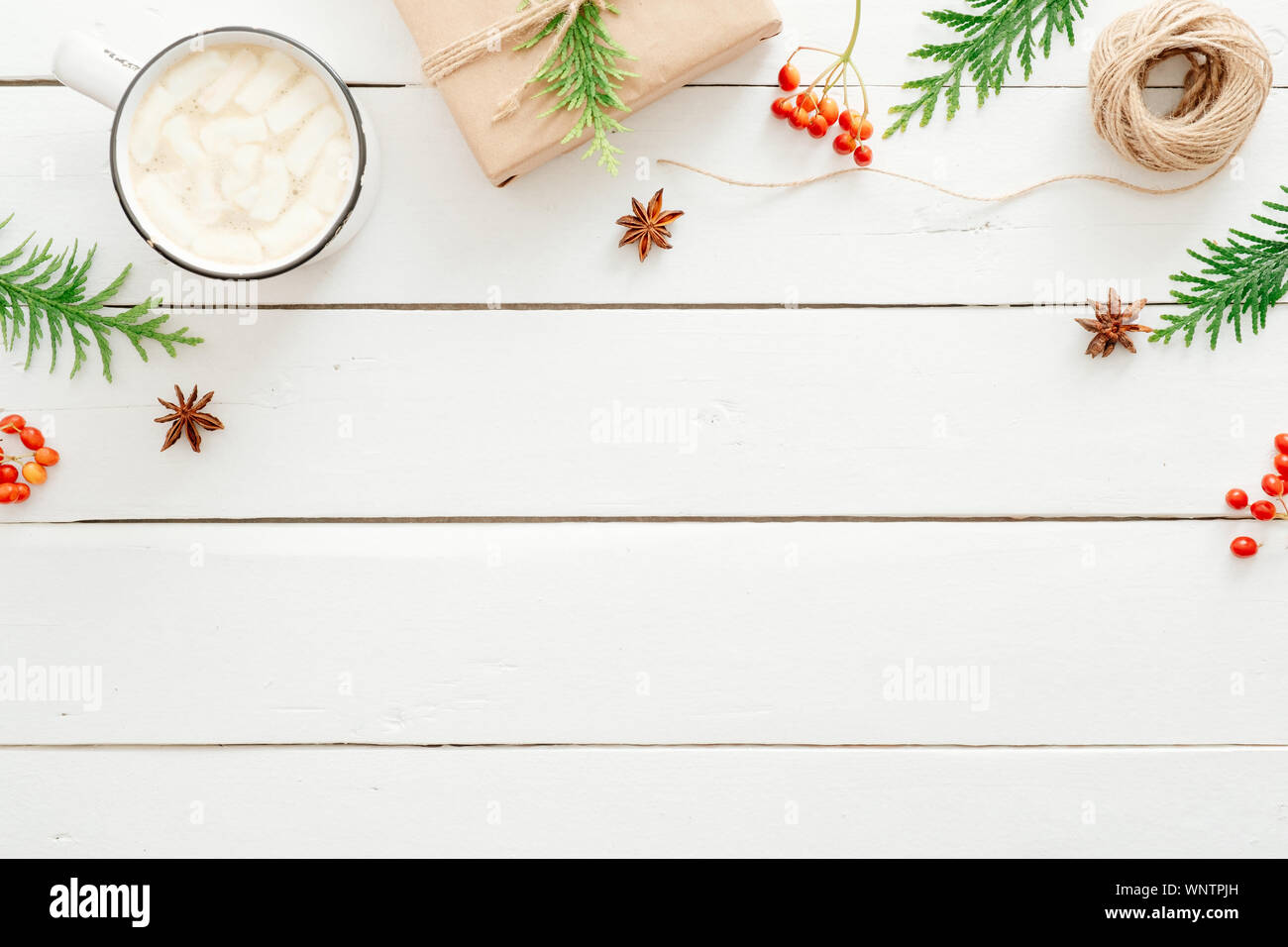 Christmas composition. Frame made of fir tree branches, gift boxes, cup of hot chocolate with marshmallow, red berry on wooden white background. Flat Stock Photo